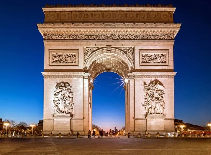 Vue frontale de l'Arc de Triomphe à Paris au crépuscule, éclairé contre un ciel bleu foncé.