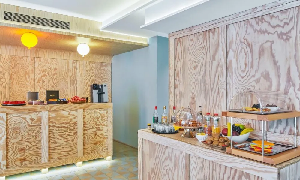 Buffet Open Bar de l’Hôtel Joke avec une sélection de boissons, viennoiseries, fruits frais et encas, dans un décor lumineux avec bois clair et design contemporain