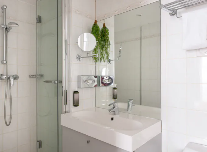Badezimmer des Doppelzimmers mit einem Waschbecken, einer Badewanne mit Dusche und einem Spiegel im Hotel George