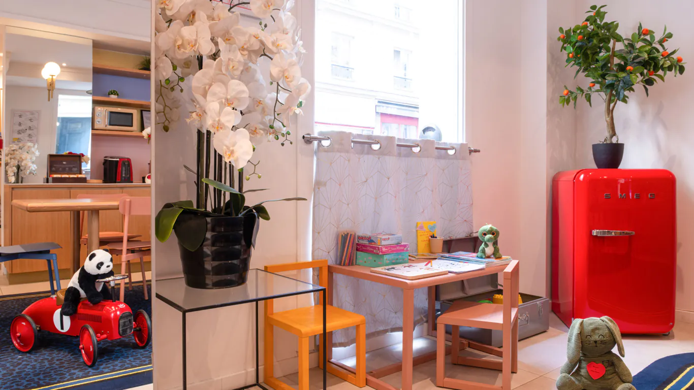 Coin enfants de l'hôtel 3 étoiles Acadia à Paris avec des couleurs douces, du mobilier adapté et des jouets ludiques.
