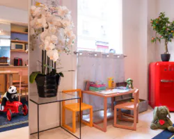 Coin enfants de l'hôtel 3 étoiles Acadia à Paris avec des couleurs douces, du mobilier adapté et des jouets ludiques.