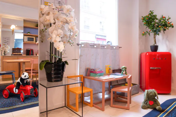 Coin enfants de l'hôtel 3 étoiles Acadia à Paris avec des couleurs douces, du mobilier adapté et des jouets ludiques.