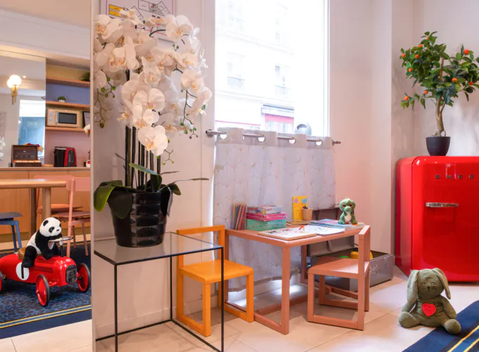 Coin enfants de l'hôtel 3 étoiles Acadia à Paris avec des couleurs douces, du mobilier adapté et des jouets ludiques.