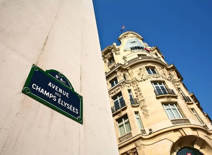 Plaque de rue de l’avenue des Champs-Élysées dans le 8e arrondissement de Paris, avec un bâtiment historique et le ciel bleu.