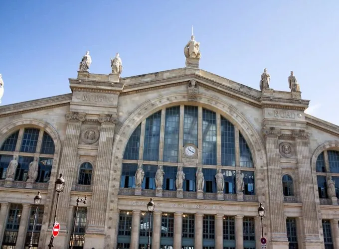 Façade monumentale de la Gare du Nord à Paris, gare historique ornée de statues et de colonnes, sous un ciel bleu.
