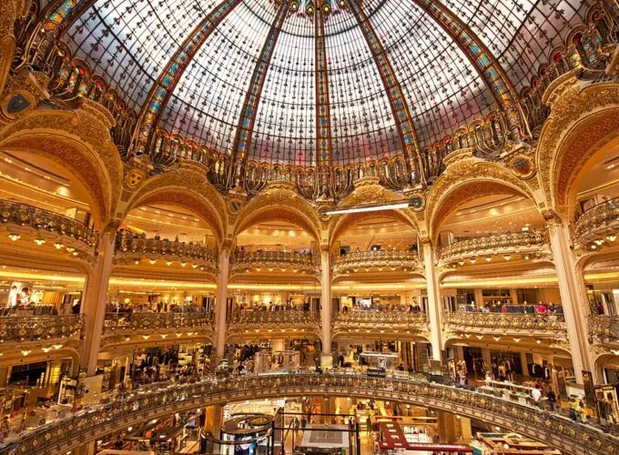Vue intérieure d’un grand magasin à Paris, avec une architecture Art nouveau, une coupole vitrée et plusieurs étages commerciaux.
