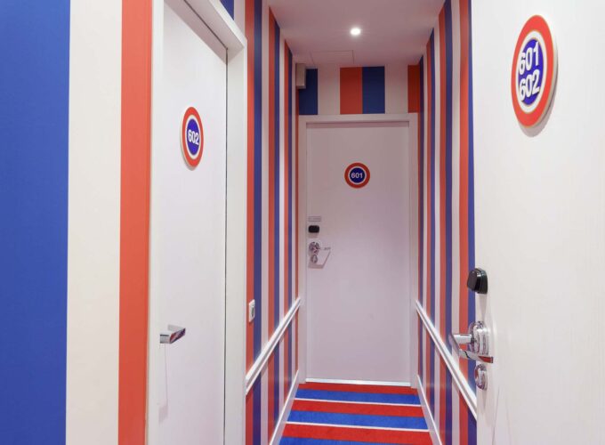 Couloir de la Chambre Familiale avec des rayures rouges, blanches et bleues et le numéro 601 sur la porte à l’Hôtel 34B