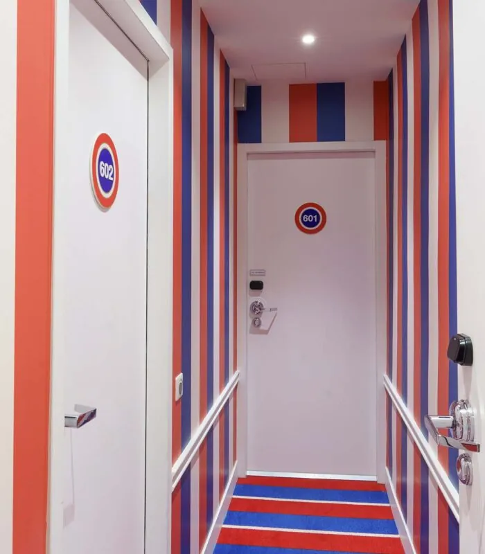 Couloir de la Chambre Familiale avec des rayures rouges, blanches et bleues et le numéro 601 sur la porte à l’Hôtel 34B