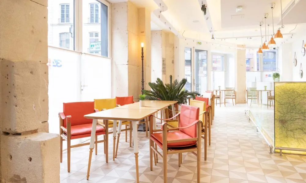 View of the Venue Marianne at Hotel 34B, a bright space with large windows, featuring wooden tables and red and yellow chairs that create a warm, colorful, and inviting atmosphere.