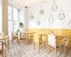 Vue de la Salle Marianne de l’hôtel 34B, un espace lumineux aux grandes fenêtres, agrémenté de tables en bois et de chaises rouges et jaunes pour une atmosphère conviviale et colorée.