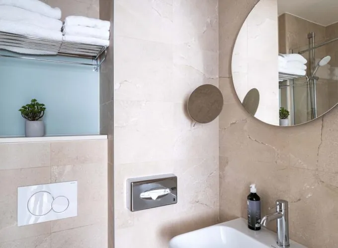Chambre Double avec salle de bain comprenant un lavabo et un miroir rond à l’hôtel Acadia