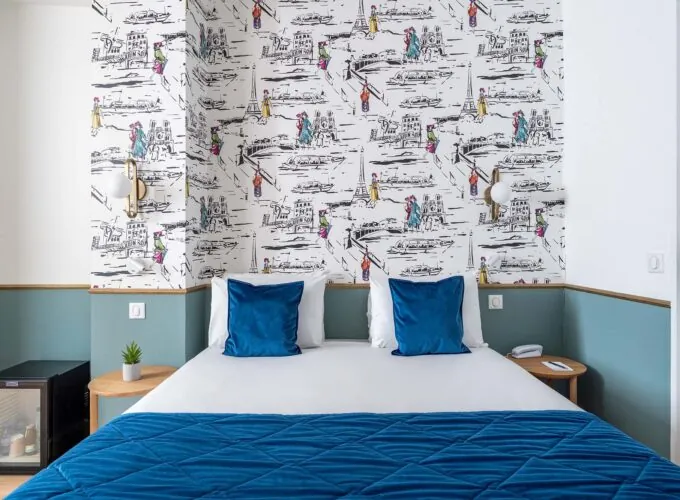 Lit d’une chambre familiale avec des oreillers bleus devant un mur décoré de dessins à l’Hôtel Acadia