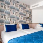 Chambre triple avec deux lits et un papier peint représentant des bâtiments à l’Hôtel Acadia