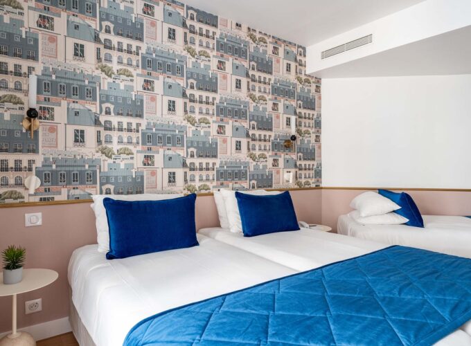 Chambre triple avec deux lits et un papier peint représentant des bâtiments à l’Hôtel Acadia