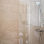 Douche d’une chambre triple avec une porte en verre transparent et une pomme de douche blanche à l’Hôtel Acadia