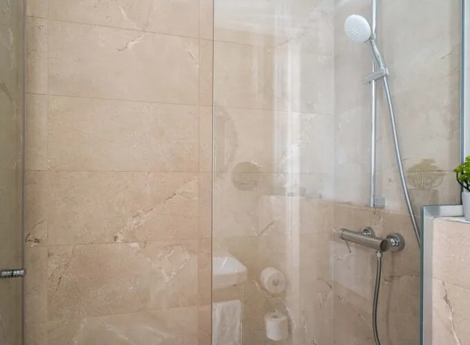 Douche d’une chambre triple avec une porte en verre transparent et une pomme de douche blanche à l’Hôtel Acadia