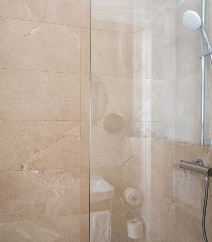 Douche d’une chambre triple avec une porte en verre transparent et une pomme de douche blanche à l’Hôtel Acadia