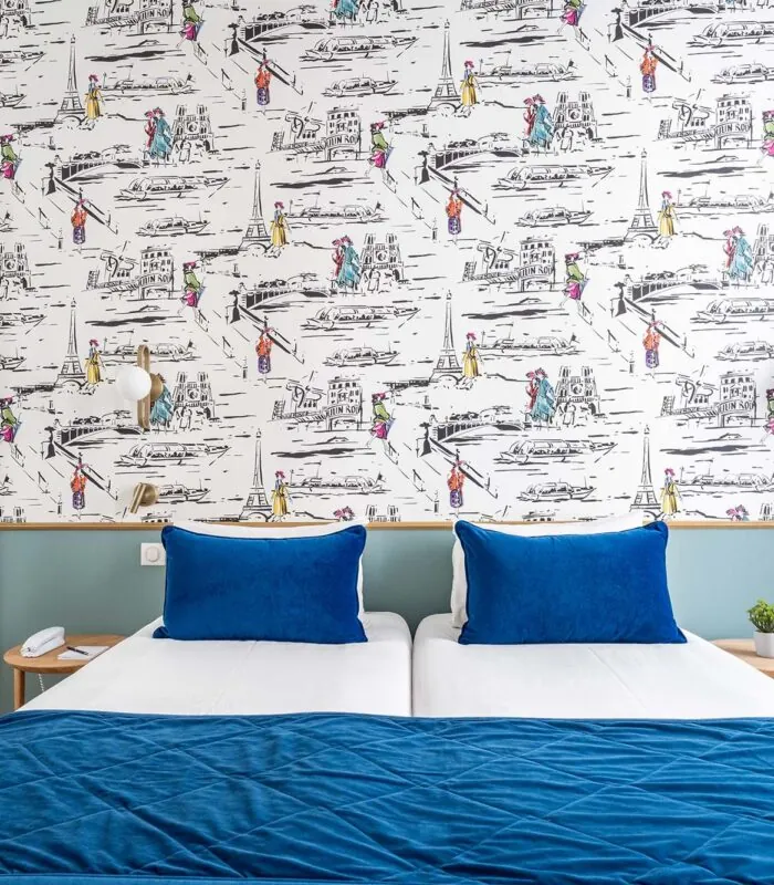 Chambre Twin avec lits et oreillers bleus devant un mur orné de dessins à l’hôtel Acadia