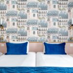 Chambre Twin avec lits et oreillers bleus devant un mur décoré de bâtiments à l’hôtel Acadia