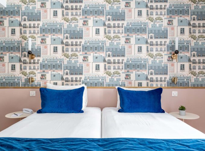 Chambre Twin avec lits et oreillers bleus devant un mur décoré de bâtiments à l’hôtel Acadia
