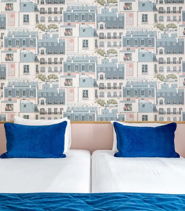 Chambre Twin avec lits et oreillers bleus devant un mur décoré de bâtiments à l’hôtel Acadia