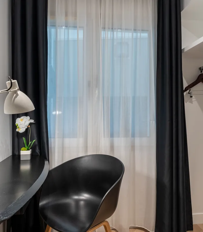 Chambre Quadruple avec une chaise noire à côté d’un bureau avec une lampe à l’hôtel Astoria