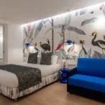 Chambre Quadruple avec un lit et une chaise avec des oiseaux sur le mur à l’hôtel Astoria