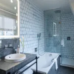 Salle de bain Exécutive Claudie Haigneré avec des carreaux bleus et une baignoire à l’hôtel Astra Opéra