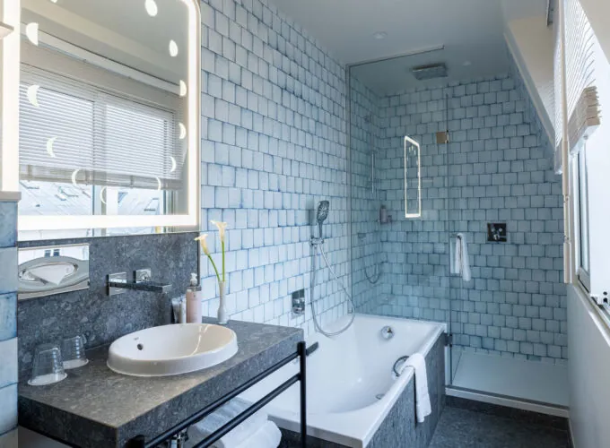 Salle de bain Exécutive Claudie Haigneré avec des carreaux bleus et une baignoire à l’hôtel Astra Opéra
