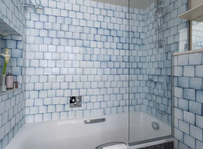 Salle de bain de la chambre Triple Claudie Haigneré avec des carreaux bleus et blancs et une baignoire à l’hôtel Astra Opéra