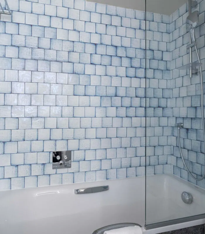 Salle de bain de la chambre Triple Claudie Haigneré avec des carreaux bleus et blancs et une baignoire à l’hôtel Astra Opéra