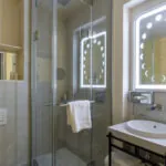 Salle de bain Twin Standard Daniel Auteuil avec un lavabo, un miroir et une douche à l’hôtel Astra Opéra