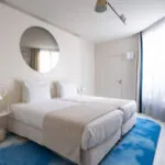 Chambre Twin Supérieure Claudie Haigneré avec deux lits et un tapis bleu à l’hôtel Astra Opéra