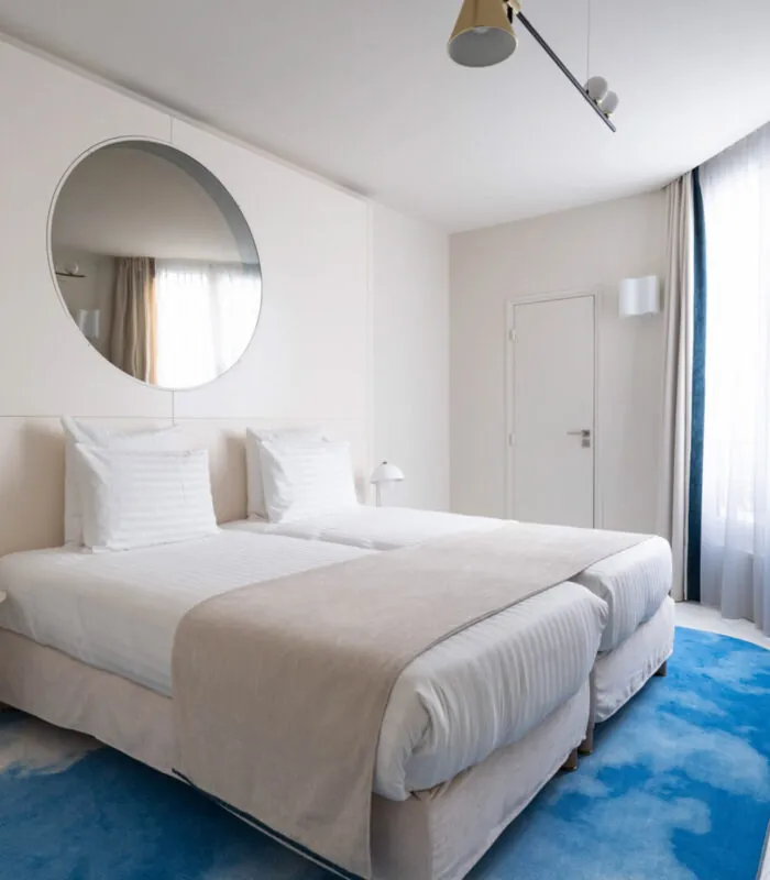 Chambre Twin Supérieure Claudie Haigneré avec deux lits et un tapis bleu à l’hôtel Astra Opéra