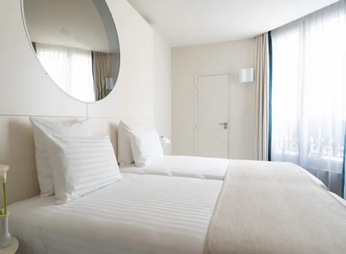 Chambre Twin Supérieure Claudie Haigneré avec deux lits et un grand miroir à l’hôtel Astra Opéra