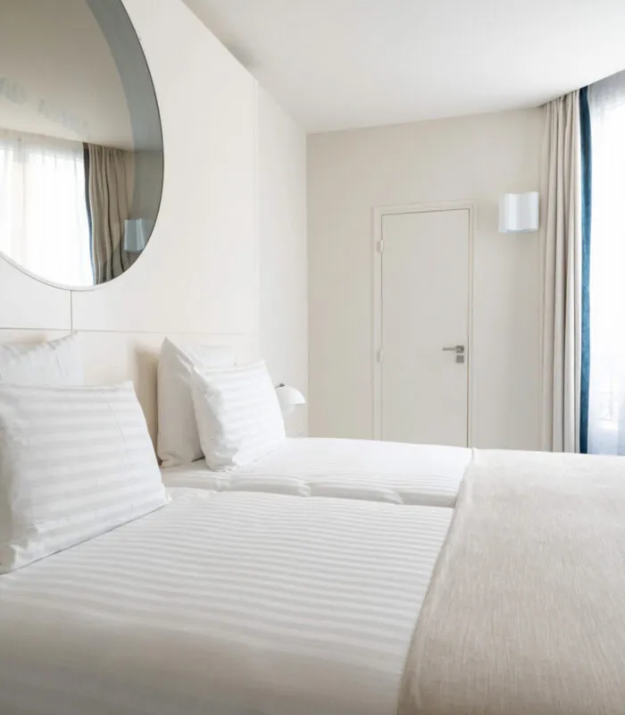 Chambre Twin Supérieure Claudie Haigneré avec deux lits et un grand miroir à l’hôtel Astra Opéra