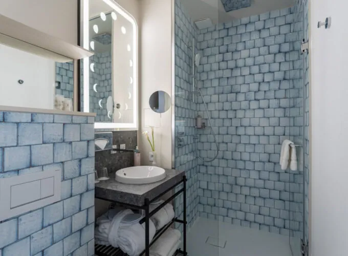 Salle de bain Twin Supérieure Claudie Haigneré avec des carreaux bleus, un lavabo et une douche à l’hôtel Astra Opéra