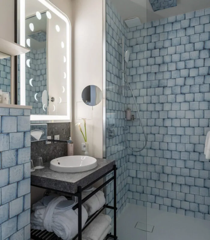 Salle de bain Twin Supérieure Claudie Haigneré avec des carreaux bleus, un lavabo et une douche à l’hôtel Astra Opéra