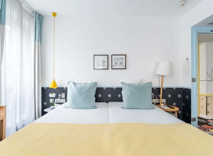 Chambre Familiale avec un lit et deux tableaux accrochés au mur à l’hôtel Augustin