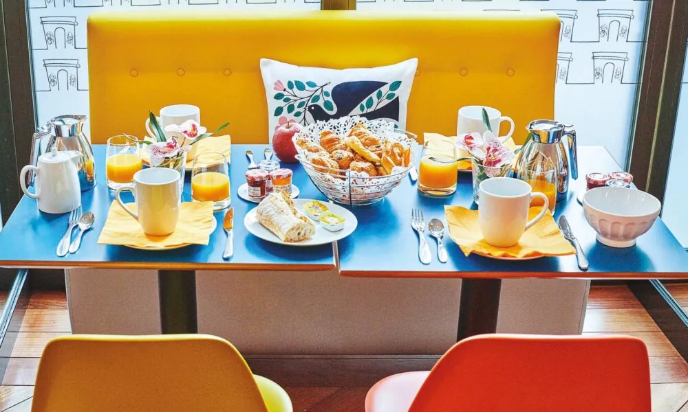 Salle de petit-déjeuner de l’hôtel Augustin à Paris avec buffet varié, atmosphère chaleureuse et touches de couleurs vives