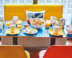 Salle de petit-déjeuner de l’hôtel Augustin à Paris avec buffet varié, atmosphère chaleureuse et touches de couleurs vives