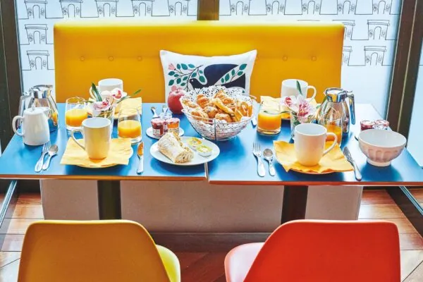Salle de petit-déjeuner de l’hôtel Augustin à Paris avec buffet varié, atmosphère chaleureuse et touches de couleurs vives