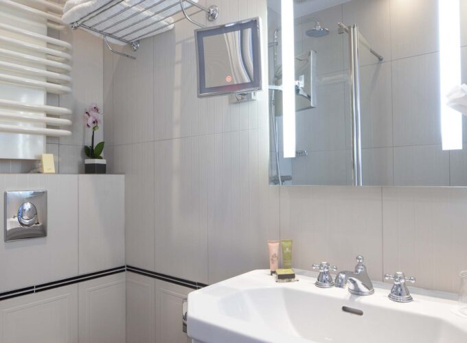 Salle de bain de la chambre Single avec un lavabo, un miroir et une douche à l’hôtel Bradford Elysées