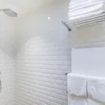 Appartement salle de bain avec des carreaux blancs et une pomme de douche à l’hôtel George