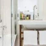Salle de bain de la Chambre Privilège à l’hôtel Joke avec un lavabo et un miroir sur lequel se trouvent des bouteilles de shampooing et d’après-shampooing