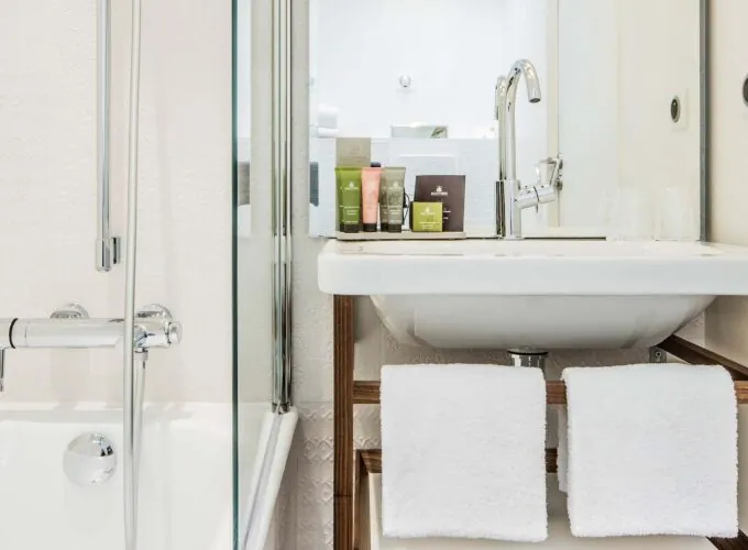 Salle de bain de la Chambre Privilège à l’hôtel Joke avec un lavabo et un miroir sur lequel se trouvent des bouteilles de shampooing et d’après-shampooing