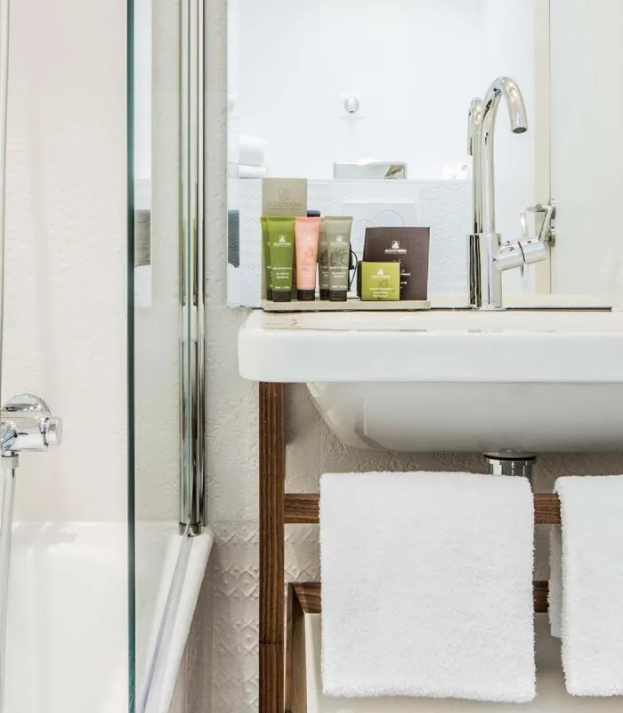 Salle de bain de la Chambre Privilège à l’hôtel Joke avec un lavabo et un miroir sur lequel se trouvent des bouteilles de shampooing et d’après-shampooing