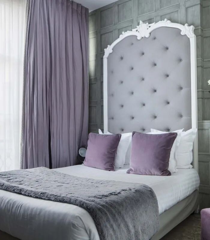 Un lit avec des oreillers violets et une tête de lit blanche à l’Hôtel Le 123 Sébastopol