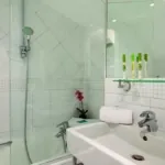 Salle de bain d’un Appartement avec un lavabo et une douche, avec des bouteilles vertes sur l’étagère, à l’Hôtel Lorette
