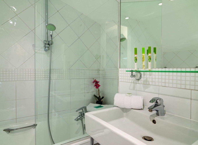 Salle de bain d’un Appartement avec un lavabo et une douche, avec des bouteilles vertes sur l’étagère, à l’Hôtel Lorette
